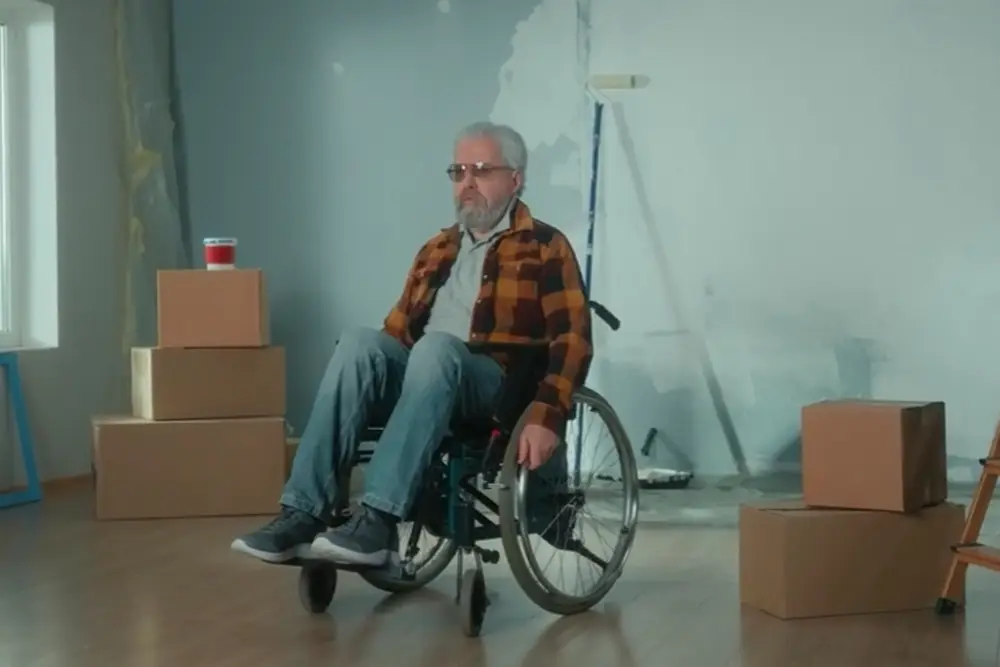 Älterer Mann bewegt sich in einem Rollstuhl mit einem Umzugskarton